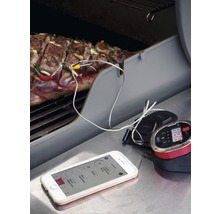 Grillthermometer in gebruik met vlees op de grill en smartphone-app voor temperatuurmonitoring
