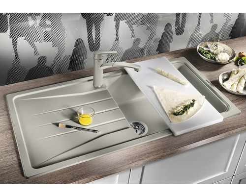 Keukenspoelbak met kraan, snijplank en eten op een aanrecht.