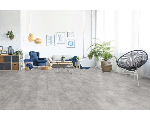 Lichte woonkamer met grijze houtlook vloer, bank, fauteuil en kamerplanten.