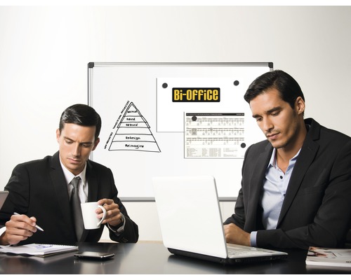 Twee mannen zitten aan een tafel met een laptop voor een whiteboardpresentatie op kantoor.