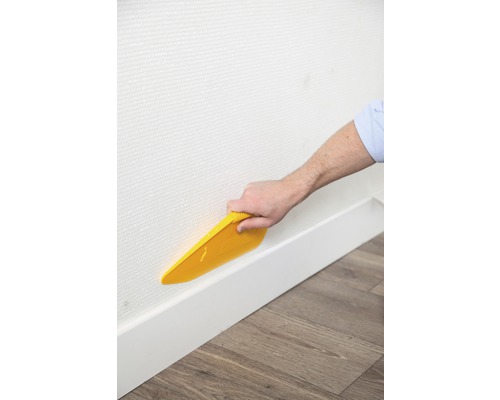 Iemand maakt behang glad op een muur met een behangspatel.