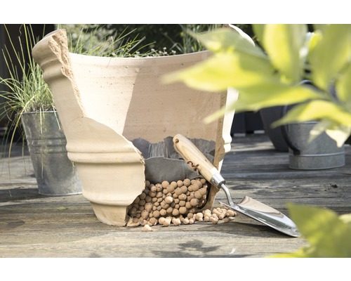 Beschadigde terracotta plantenpot met kleikorrels en plantschep