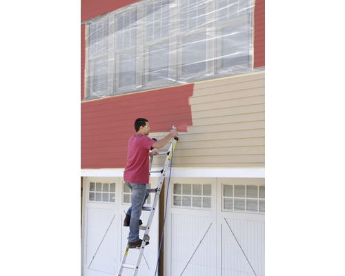 Man schildert de gevel van een huis met een verfspuit vanaf een ladder. De ramen zijn afgedekt met folie.