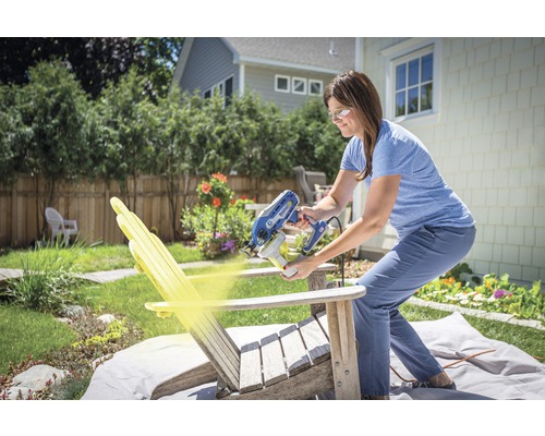 Vrouw spuit houten stoel met verfspuit in de tuin.