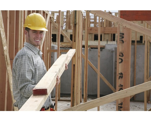 Een bouwvakker met veiligheidshelm houdt houten latten vast op een bouwplaats.