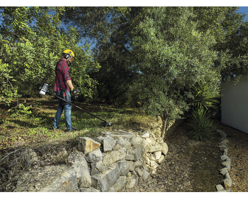 Een man gebruikt een grastrimmer in de tuin om het gras te maaien.
