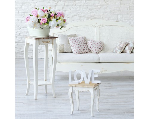 Decoratief interieur met bloemstuk, bijzettafels, kussens en een bank.