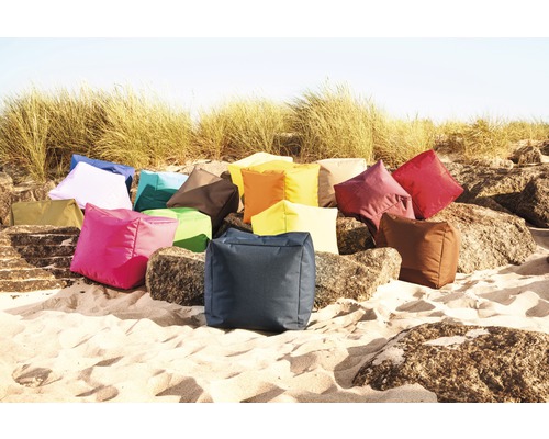 Een verzameling vierkante kussens in verschillende kleuren op zand en rotsen.