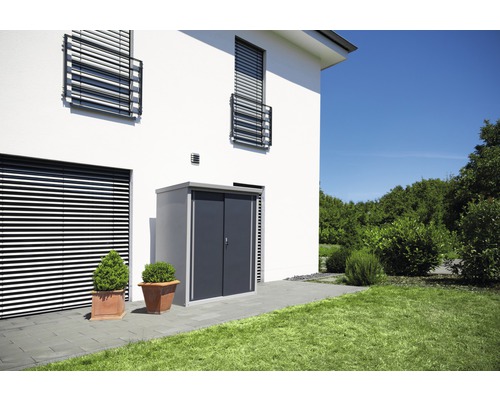 Metalen tuinhuis met schuifdeur naast een modern huis met jaloezieën