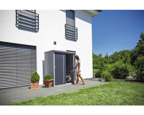 Vrouw betreedt tuinhuis met slangentrommel voor wit huis