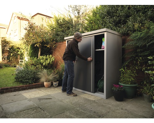 Man opent tuinkast met schuifdeuren voor het opbergen van tuingereedschap in de tuin.