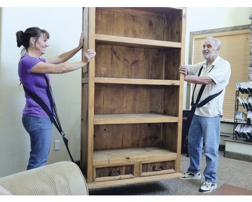 Twee personen verplaatsen een houten boekenkast met draagriemen.