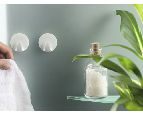 Twee ronde, witte zelfklevende haken aan een badkamermuur, met een handdoek en decoratie