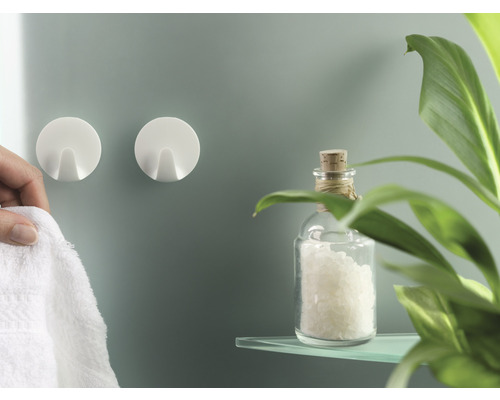 Twee ronde wandhaken en een persoon hangt er een handdoek aan, samen met een glazen fles en een plant op een plank