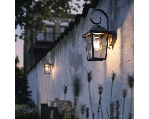 Buitenwandlampen aan een muur verlichten een tuingedeelte.