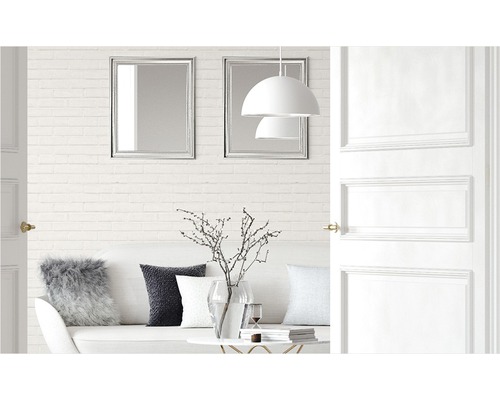 Lichte woonkamer met bank, kussens, tafel, decoratie, lampen, spiegels en open deur.