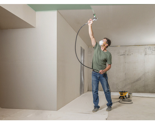 Man schildert plafond met verfspuit in een ruimte.