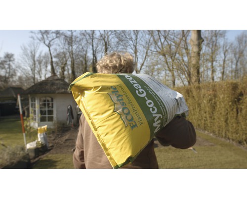 Man draagt zak met gazonzaden in de tuin