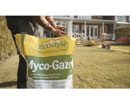 Een man strooit gazonmeststof van Ecostyle op een gazon