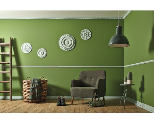 Woonkamer met fauteuil, lamp, ladder en decoratieve artikelen tegen een groene wand