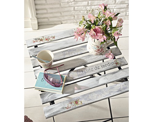 Decoratieve tuintafel met vaas met bloemen, kop, boek en bril