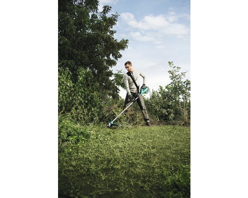 Een man gebruikt een grastrimmer in een tuin om het gazon te maaien.