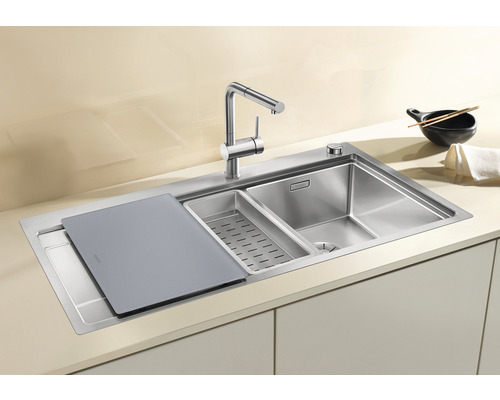 Roestvrijstalen gootsteen met snijplank, afdruipbak en keukenkraan op een aanrecht.