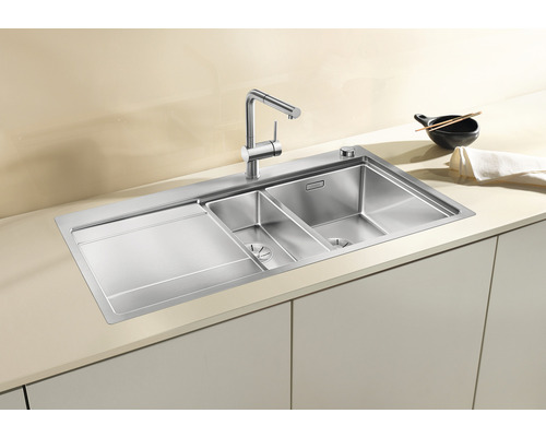 Roestvrijstalen spoelbak met afdruiprek en twee wasbakken in een lichte keuken.