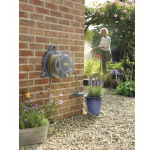 Wandslangenbox met tuinslang in een tuin met een vrouw die bloemen water geeft.