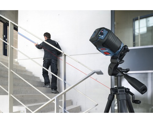 Bouwplaats met lijnlaser op statief en vakman op trap