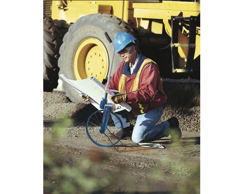 Een arbeider met bouwtekening en meetwiel voor een graafmachine.