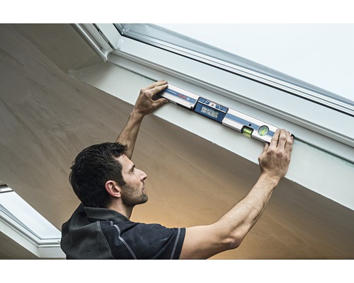 Ambachtsman gebruikt een digitale waterpas op een dakraamkozijn.