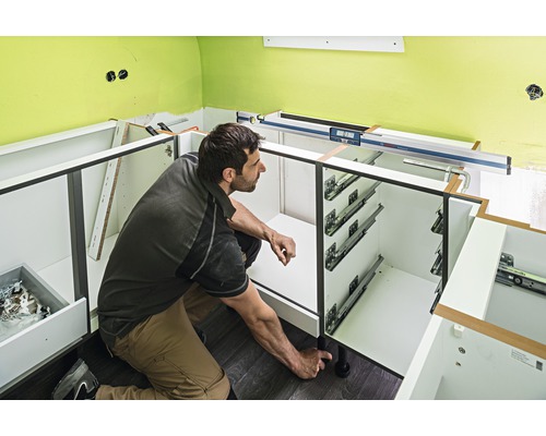 Een man monteert keukenkasten met uittrekelementen en verstelbare poten.