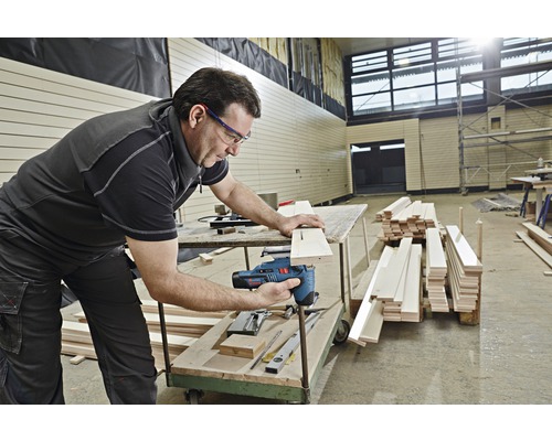 Een man gebruikt een decoupeerzaag om een houten plank te zagen.