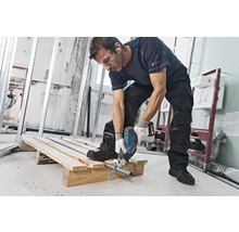Een man zaagt met een reciprozaag een buis door op een houten pallet op een bouwplaats.