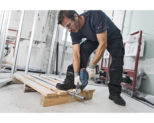 Een man zaagt met een reciprozaag een buis door op een houten pallet op een bouwplaats.