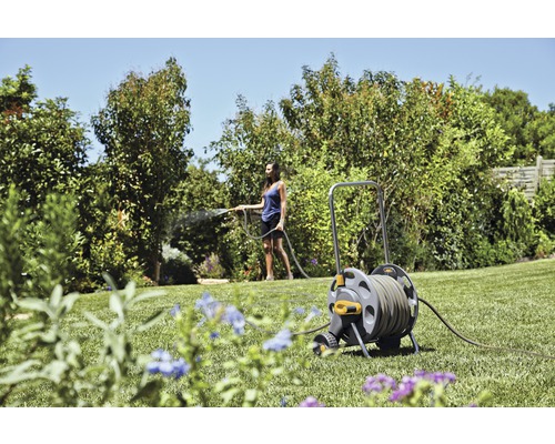 Tuinscene met een vrouw die een gazon besproeit met een slang en haspelwagen