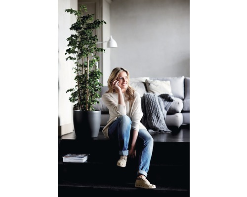 Lichte, vriendelijke woonkamer met een vrouw zittend op een trap, een kamerplant in een pot en een bank