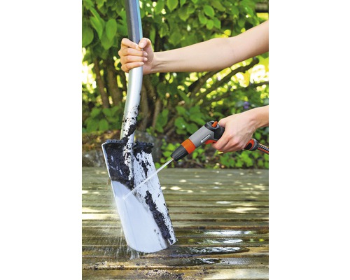Een persoon maakt een spade schoon met een waterstraal op een houten oppervlak.