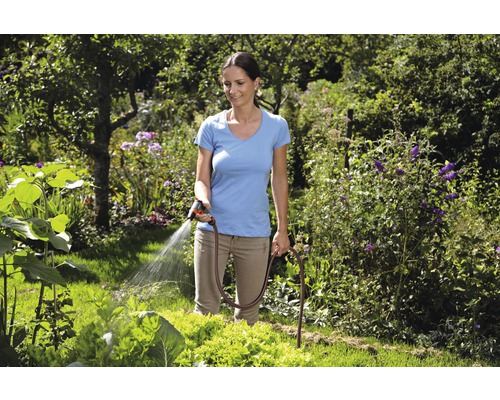 Vrouw besproeit tuin met tuinslang en spuitpistool