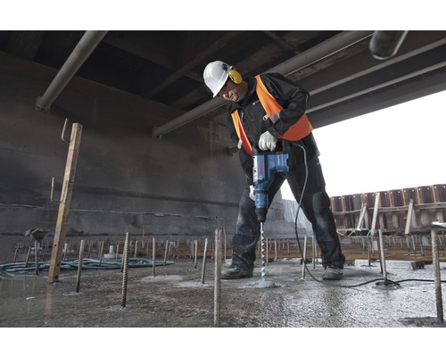Een bouwvakker boort met een boorhamer in beton