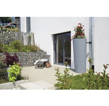 Regenwatertank met beplanting naast een huis met terras en ligstoel