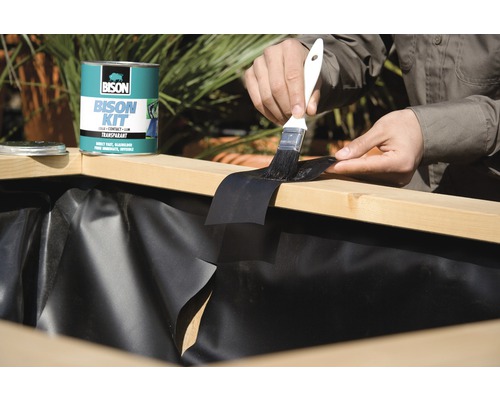 Buitenopname van een persoon die vijverfolie met Bison Kit lijm en een kwast op een stuk hout lijmt.