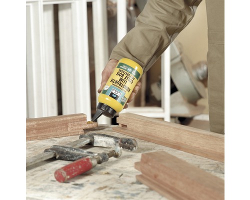 Iemand brengt houtlijm aan op een stuk hout. Een lijmklem en een hamer zijn ook zichtbaar op de afbeelding.