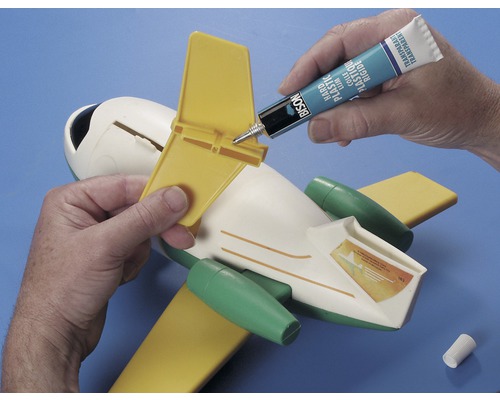 Een persoon lijmt een geel staartstuk op een speelgoedvliegtuig met lijm.
