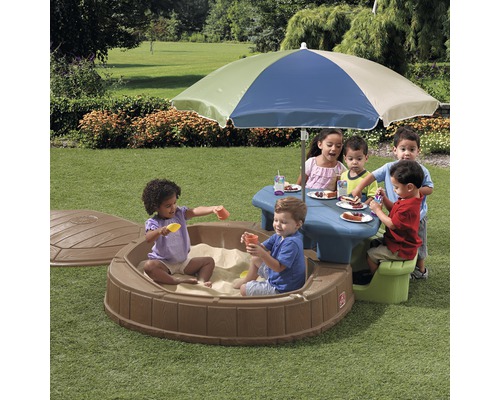 Speelruimte voor kinderen met zandbak, picknicktafel en parasol in de tuin.