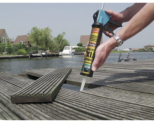 Iemand gebruikt Bison montagelijm op een houten terras aan het water.