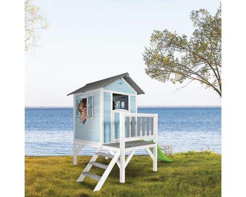 Speelhuis met glijbaan, trap en raam op een gazon voor een meer