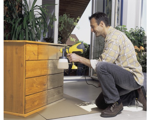 Een man spuit met een verfspuit een houten commode.