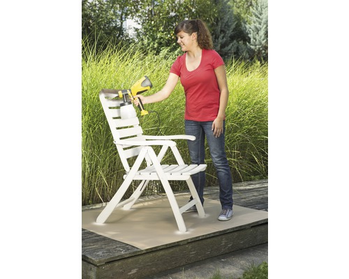 Vrouw schildert een houten stoel met een verfspuitpistool in de tuin.